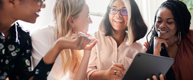 Four women professionals standing at table discussing work